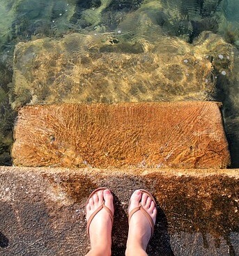 A pair of feet wearing sandals by the sea
